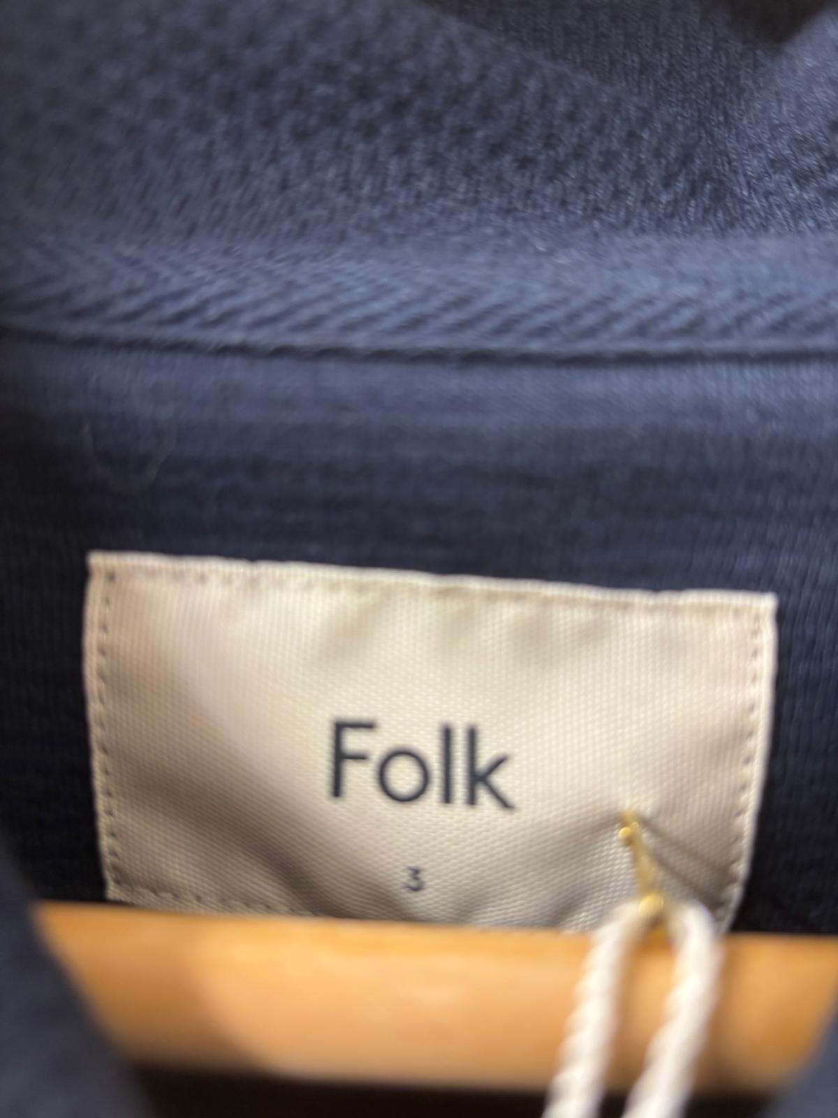 Close-up of a blue fabric with a 'Folk' label on a hanger.