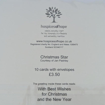 A white postcard from House of Cards, featuring Christmas Star 2024, photographed on a light brown wooden surface inside a clear protective sleeve.
