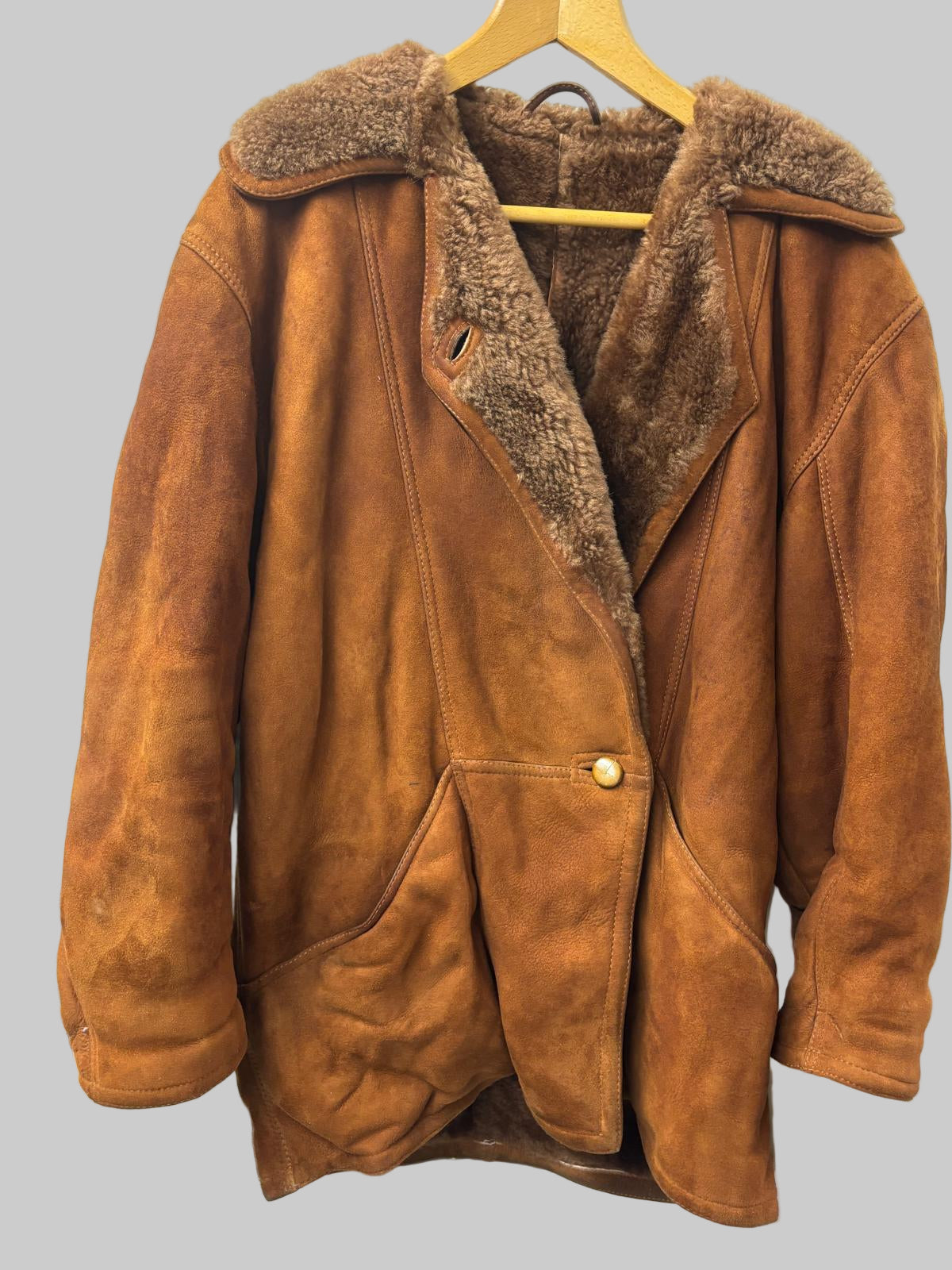 Brown leather jacket with fur lining on a hanger against a white background